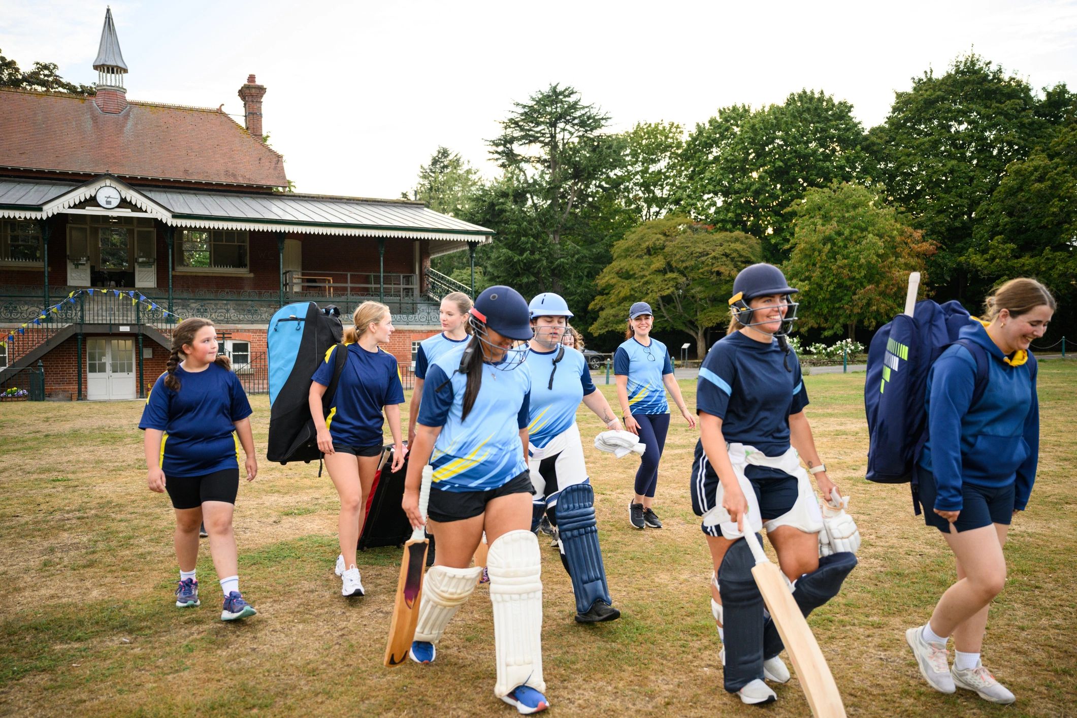Women and girls cricket teams walking on to the field to practise